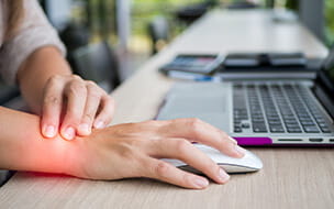 Closeup of a woman holding her wrist from pain using her computer