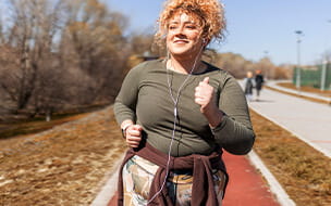 Woman with curly hair running on a sunny day with headphones