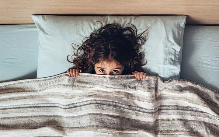 Child in bed peeking out from under covers