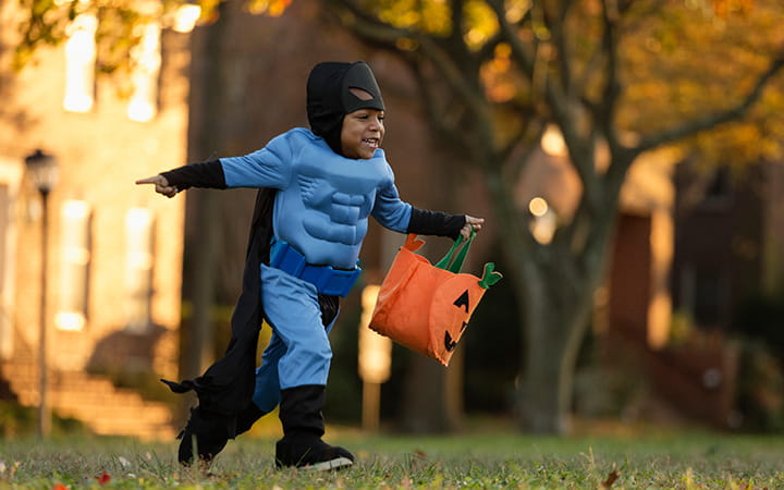 young boy in batman costume running with treat bag