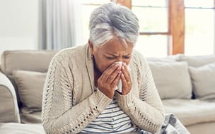 A senior woman sneezes into a tissue