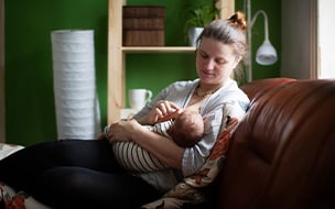 A mother feeds her newborn while sitting on a sofa at home