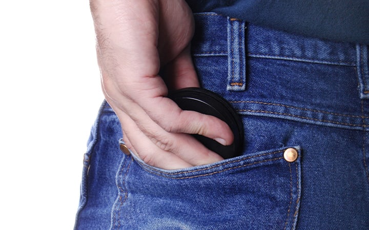 A person puts a round container in their back jeans pocket.