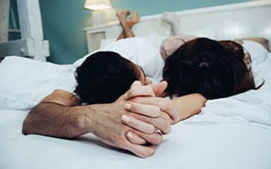 man and woman hold hands in bed