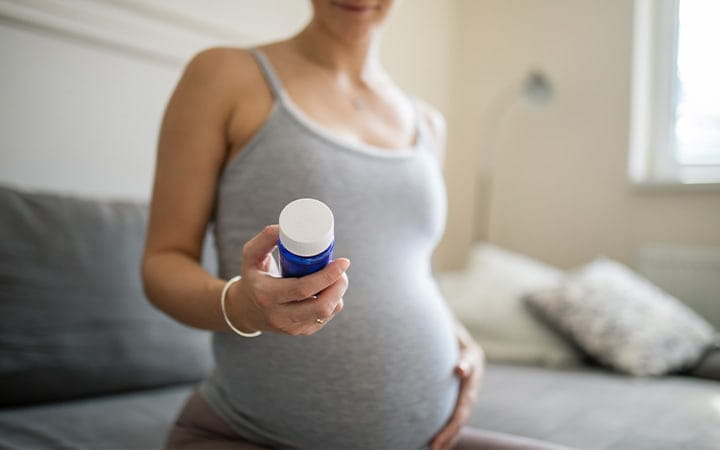 pregnant woman looks at pill bottle