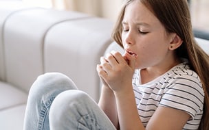 A young girl sitting on sofa, feeling bad and suffering from dry cough